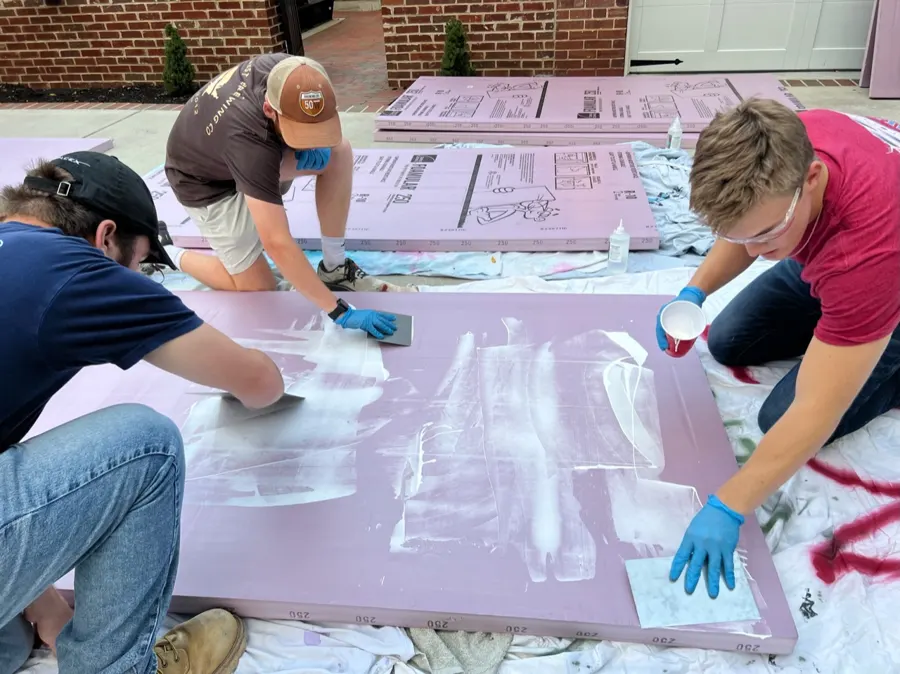 Team members spreading glue across pink XPS foam sheets.