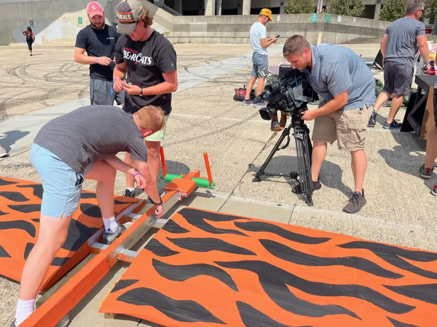 A TV camera crew filming team members painting tiger stripes on the wing.